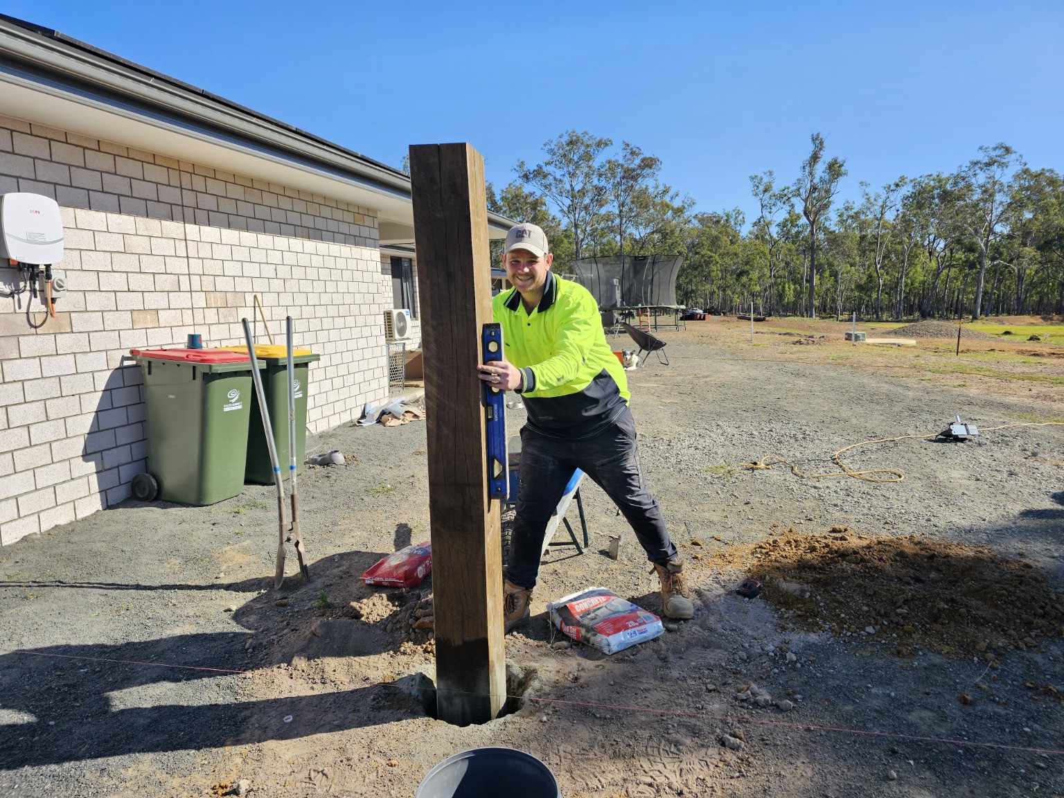 Blissful landscaper setting a timber fence post on site
